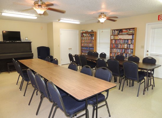Heritage Village clubroom with tables and chairs, piano, tv and bookshelf