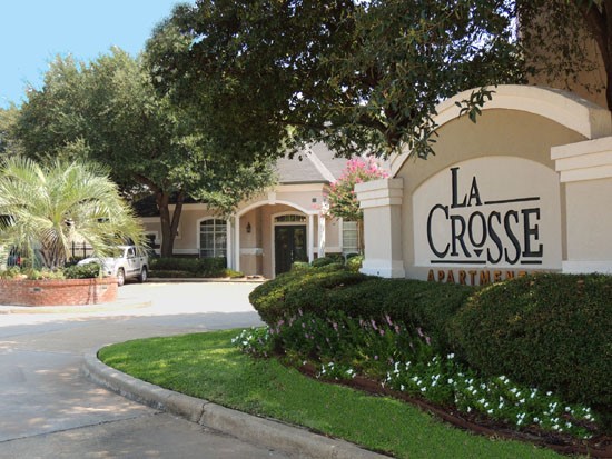 La Crosse Apartments huge white and tan front sign with black and red letters, bushes in front of sign