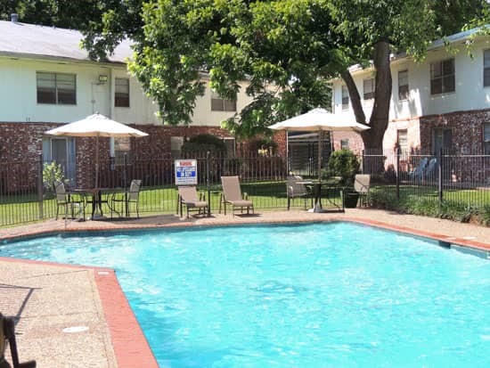 Park Villa Apartments pool side view with pool side lounge chairs and tables surrounded by fence